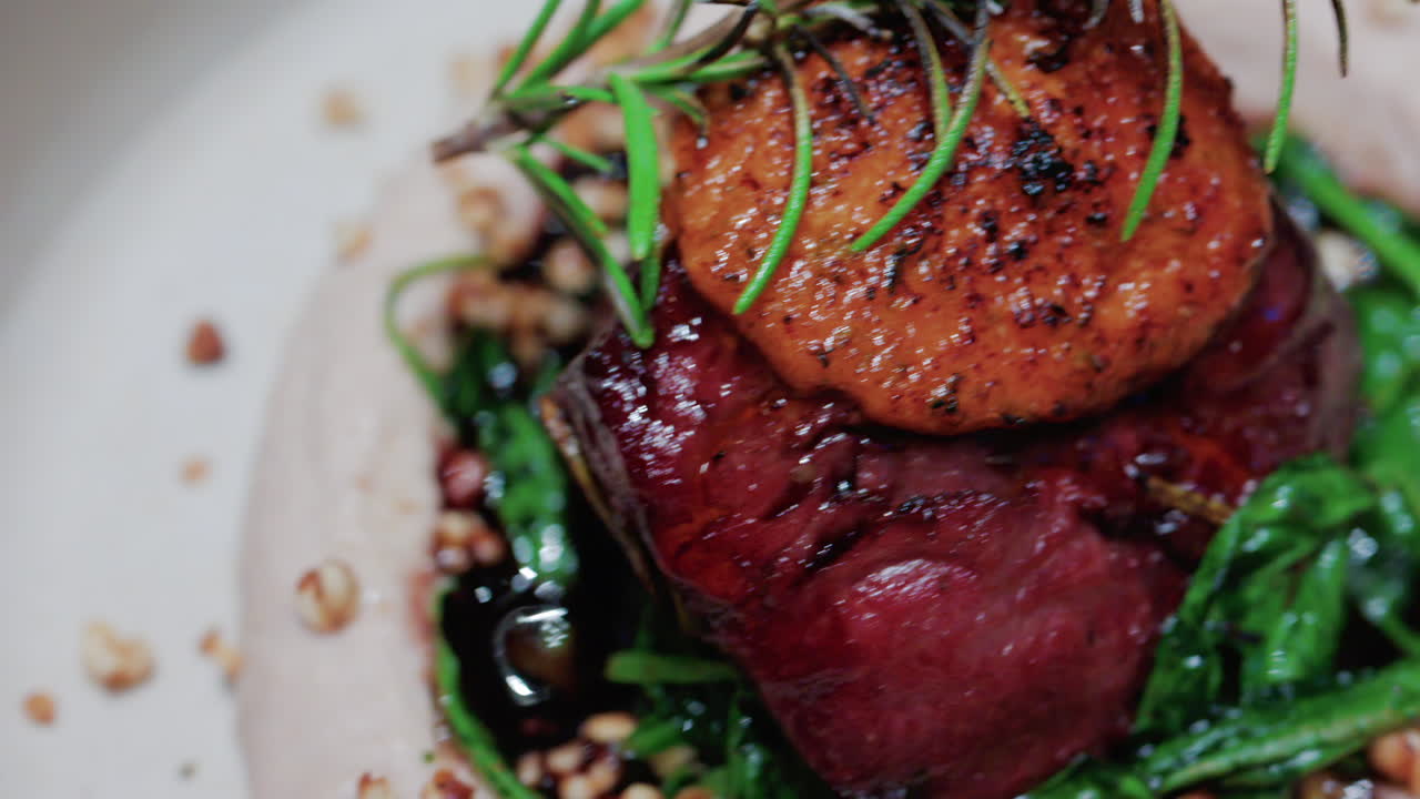 Close up of a gourmet dish featuring grilled steak topped with foie gras, served with sauteed spinach and a rosemary garnish