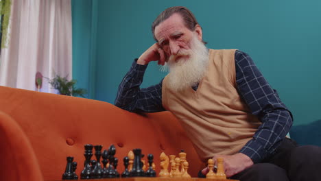 Focused-senior-grandfather-man-playing-chess-leisure-board-game-alone,-domestic-activity-at-home