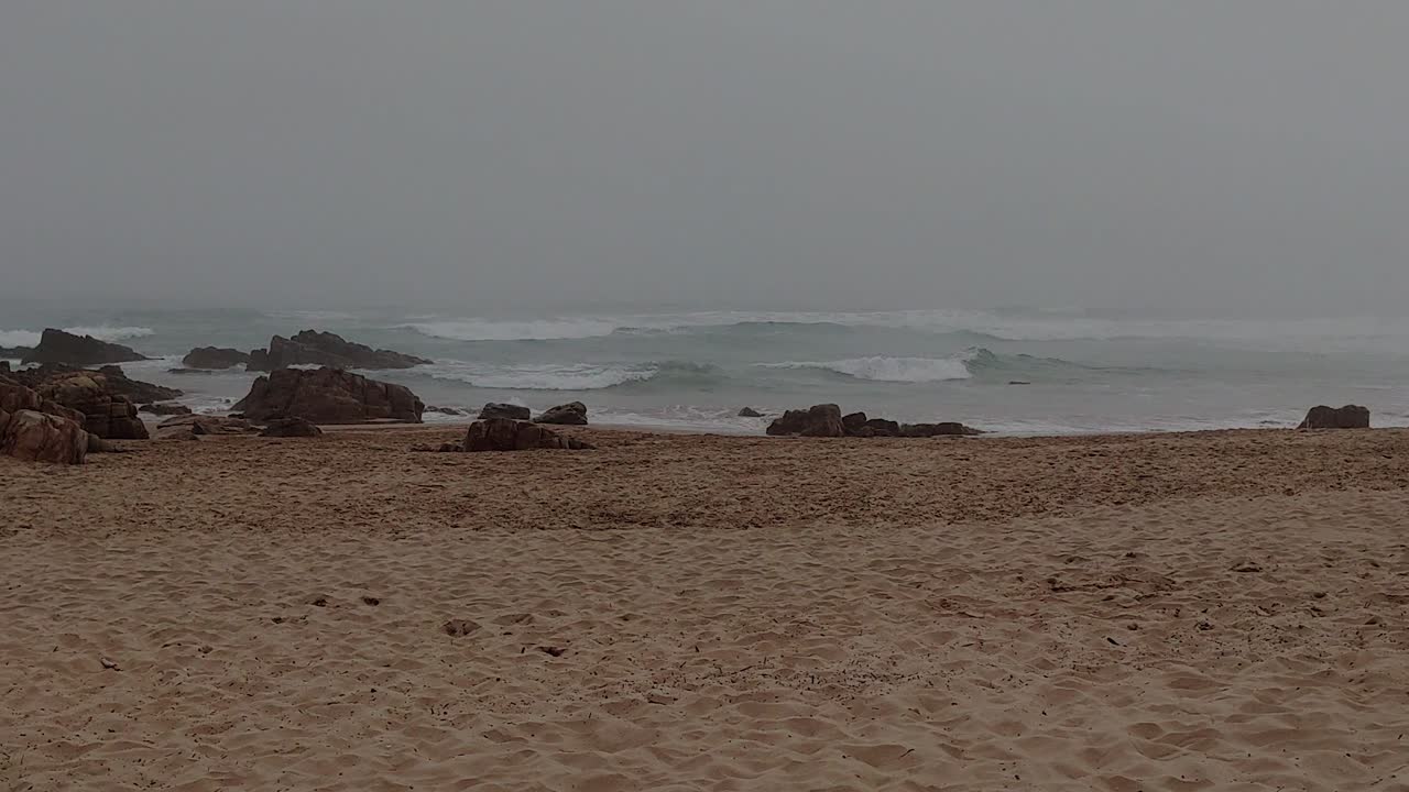 A static shot of a deserted beach on a miserable overcast and hazy day, the shoreline being battered with heavy waves as a storm approaches the coastline, Durban, South Africa