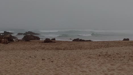 a static shot of a deserted beach on a miserable overcast and hazy day, the shoreline being battered with heavy waves as a storm approaches the coastline, durban, south africa