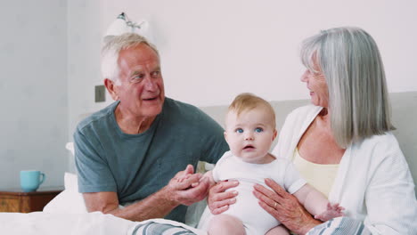 grandparents lying in bed at home looking after baby grandson