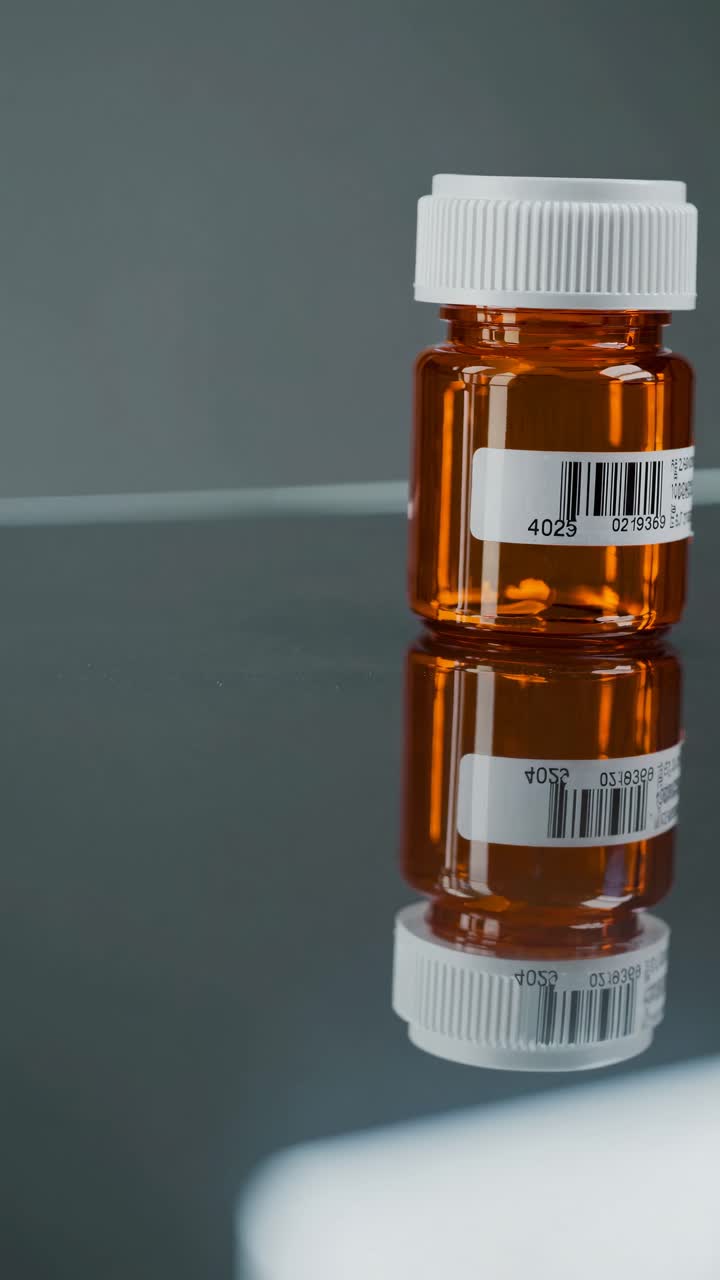 Primo piano di un video che mostra un flacone di medicinale su una superficie riflettente, ripreso da un angolo basso