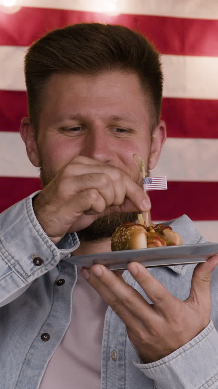 Man holding a hot dog with American flag in background