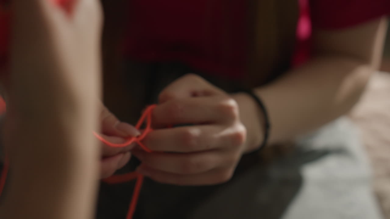 Unas manos elaboran un tejido intrincado; una persona crea un patrón con hilo; primer plano de unas manos que tejen cuidadosamente hilos de colores; toma detallada de unas manos que forman meticulosamente bucles y nudos con hilo.