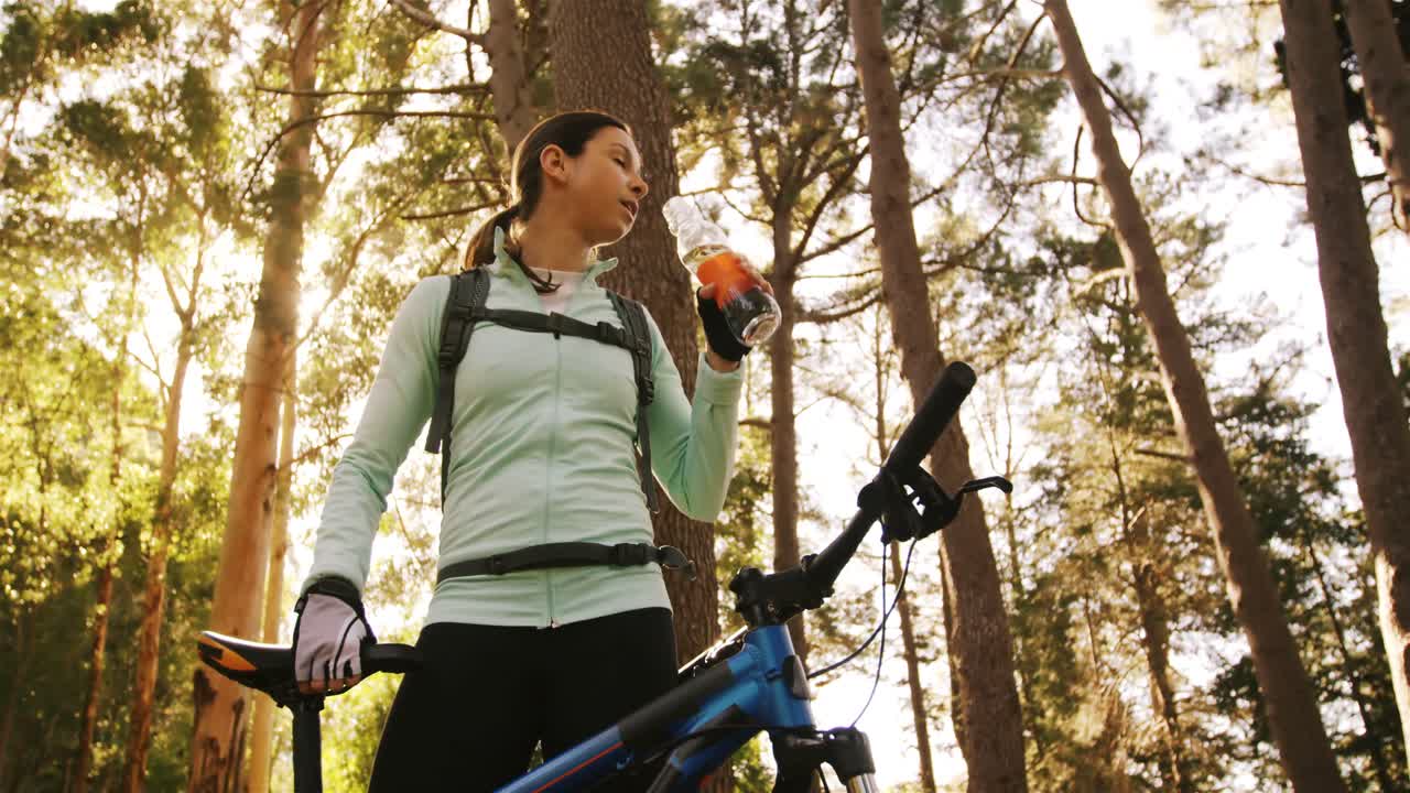 mujer ciclista de montaña bebiendo agua en el bosque