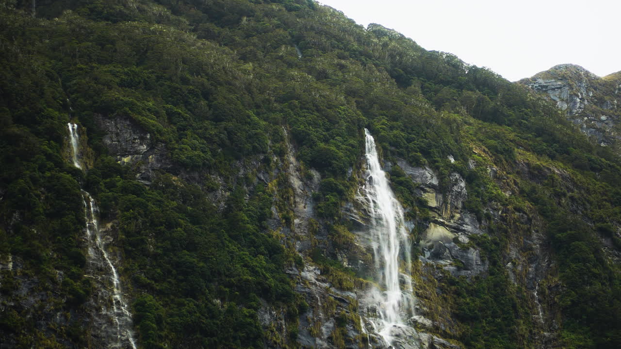 Aerial panning view of little waterfall that runs along the ridge of mountain