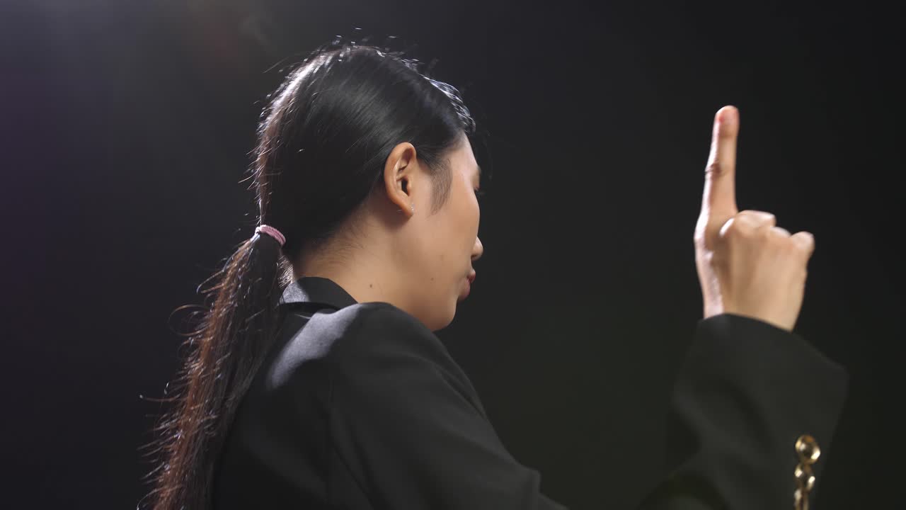 블랙 스크린 스튜디오에서 말하는 동안 지표손가락을 보여주는 비즈니스 슈트를 입은 아시아 스피커 여성의 측면 시각