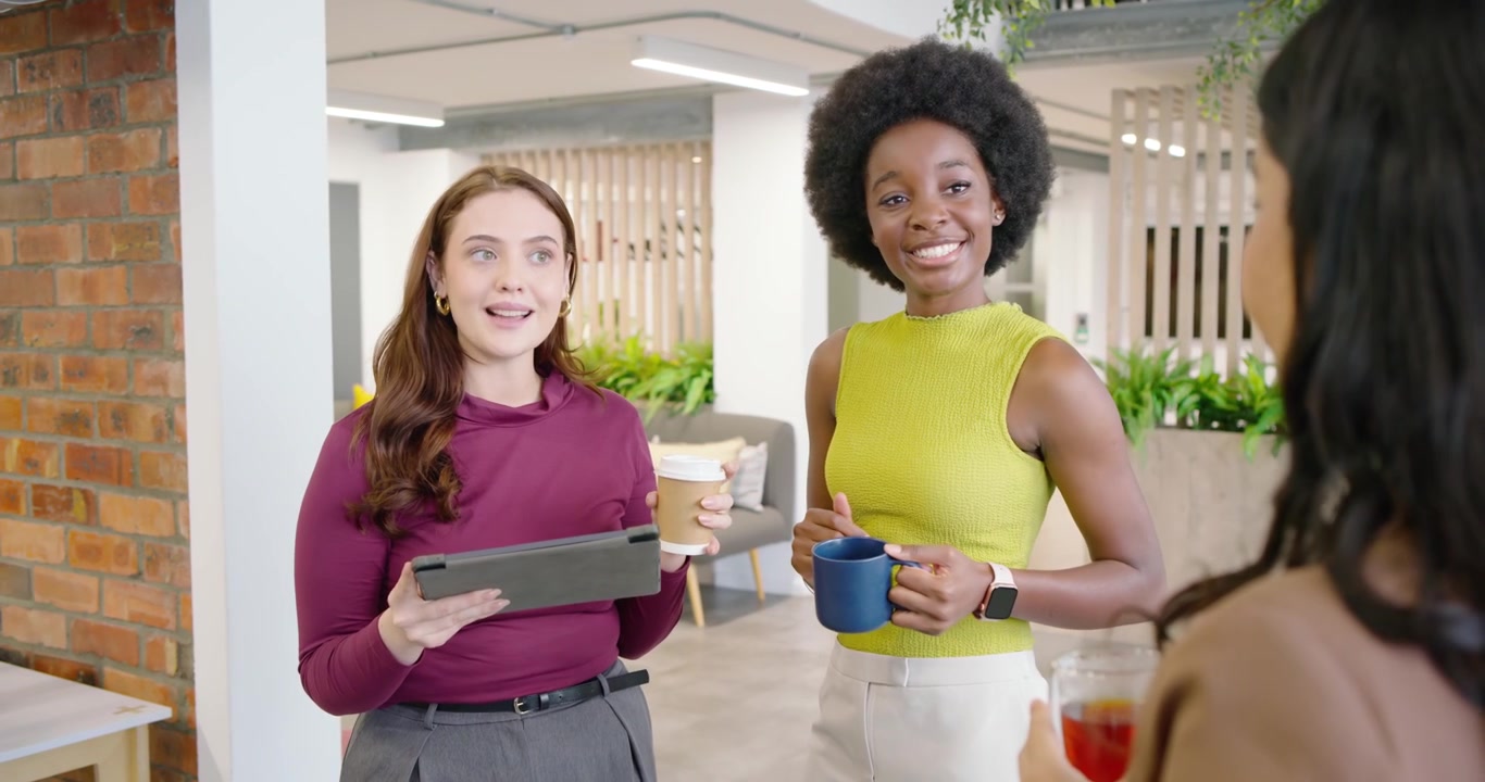 Colleghe diverse che gesticolano con un bicchiere rosso, discutendo di lavoro, usando un tablet nella lounge dell'ufficio.