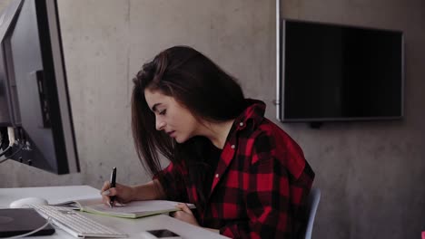 joven atractiva con camisa de franela roja escribiendo algo en su cuaderno,
