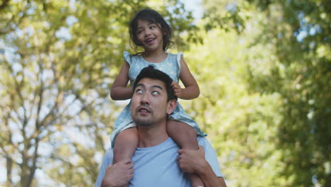 happy young asian man giving his cheerful daughter piggyback ride