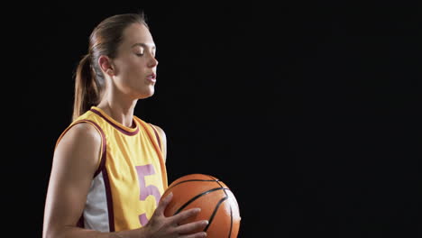 Una-Joven-Caucásica-Sostiene-Una-Pelota-De-Baloncesto-Sobre-Un-Fondo-Negro,-Con-Espacio-Para-Copiar