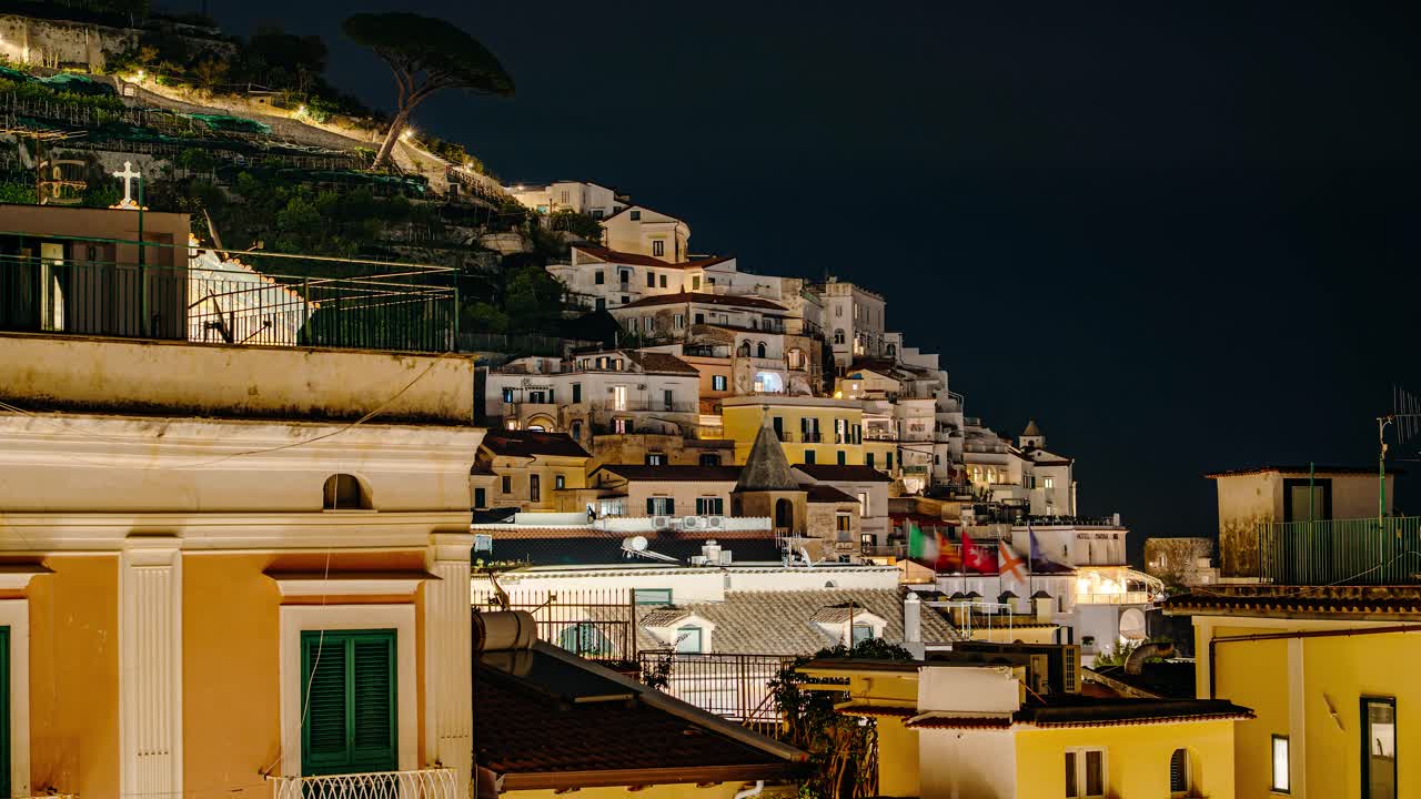 Timelapse di viaggio notturno che domina la città costiera di Amalfi con finestre illuminate, architettura a terrazze e un cielo costiero profondo. Architettura storica della città di Amalfi di notte.