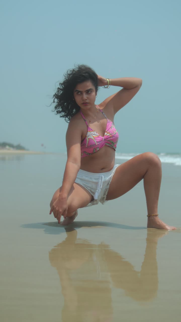 Woman drawing on wet beach sand in swimsuit and shorts on a calm sunny day