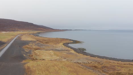 scenic iceland coastline landscape, empty road by sea seen from above, aerial drone view flying forward on cloudy day