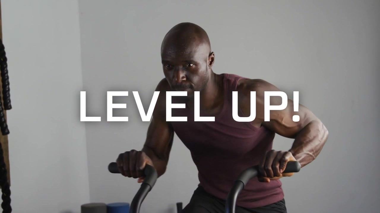 Man riding air bike in gym glitch causing LEVEL UP! text appearing over him, raising fitness