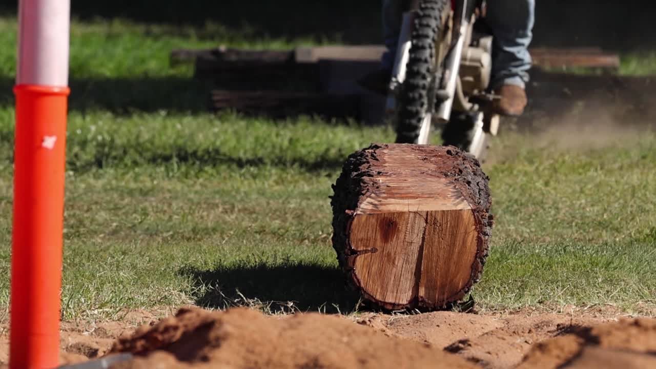 A motorbike navigates over a log obstacle on a dirt track, showcasing skill and control.