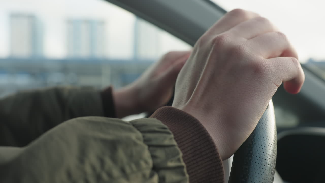 close up hand view tapping steering wheel to music with blurred city skyline through car window creating upbeat vibe in parked car scene