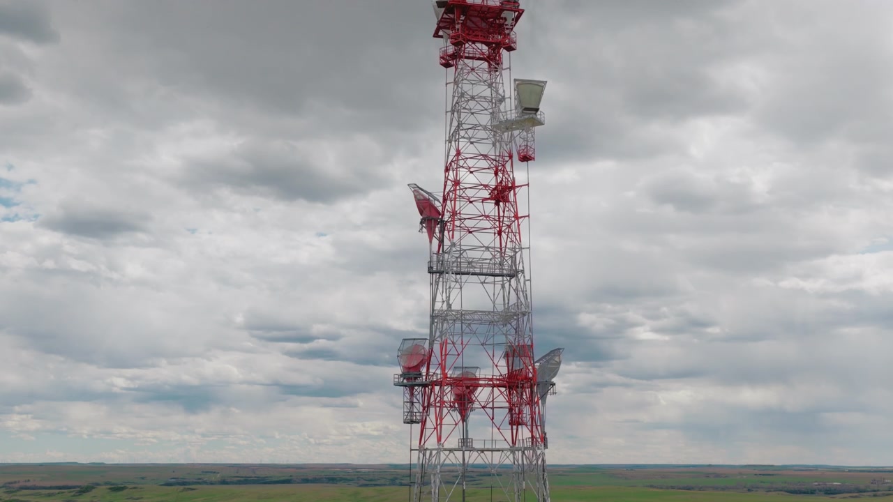 Torre di ripetizione a microonde per telecomunicazioni si erge contro un cielo coperto. Questa vista da drone mostra una struttura a traliccio vintage rossa e bianca dotata di grandi antenne a tromba nelle pianure rurali