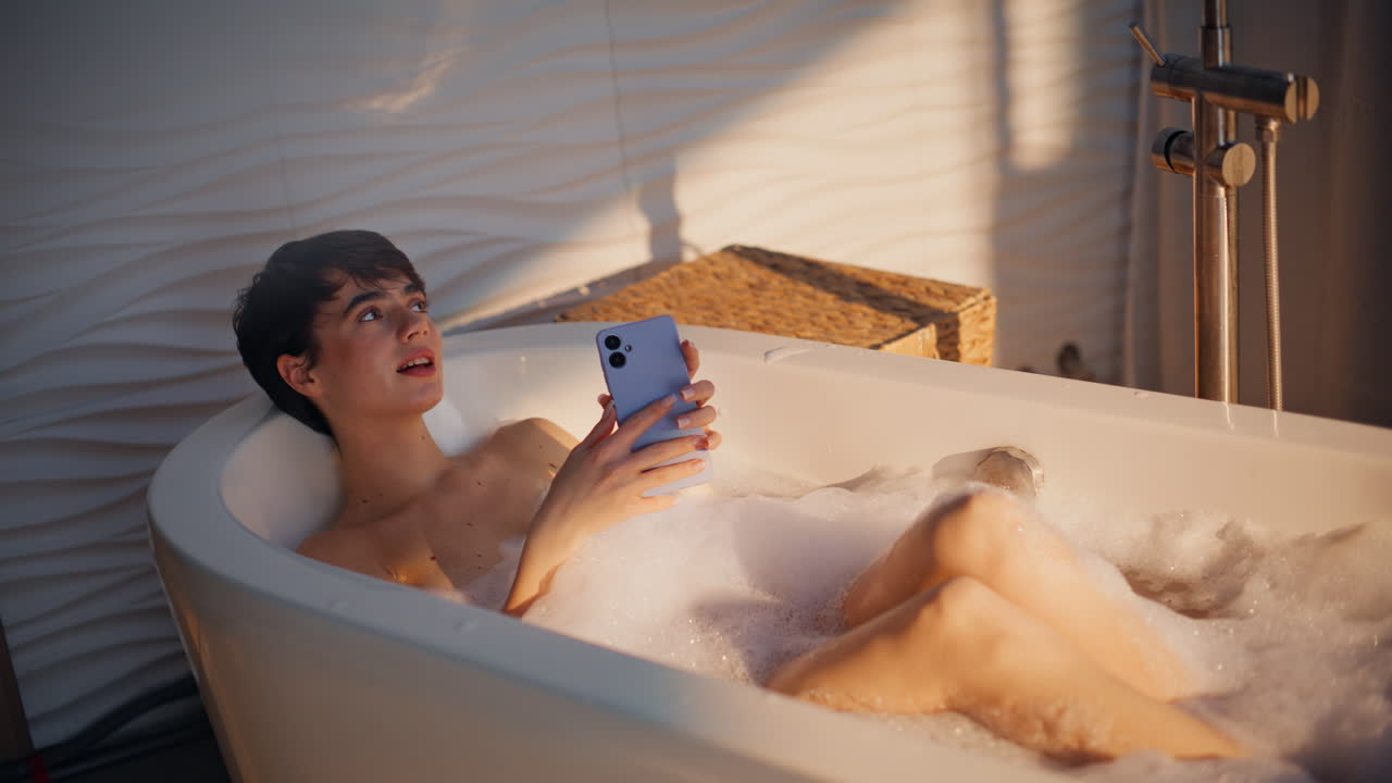 Sexy woman getting message on smartphone in hot bathtub. Self love girl chilling