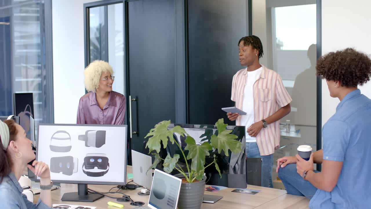 Team collaborating in office, discussing VR headset designs on computer screens