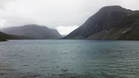 flying-over-a-large-blue-lake-in-the-middle-of-a-plain-in-a-rocky-mountain-range,-norway,-europe,-drone