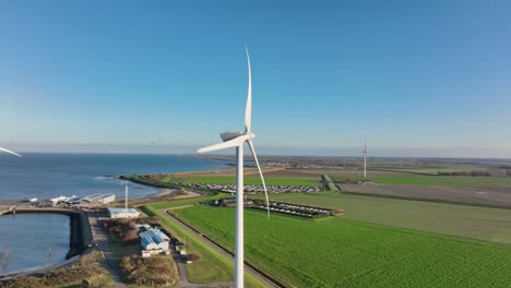 Toma-Aérea-En-Cámara-Lenta-De-Turbinas-Eólicas-En-Una-Zona-Rural-De-Los-Países-Bajos-Contra-Un-Cielo-Azul-En-Un-Día-Soleado