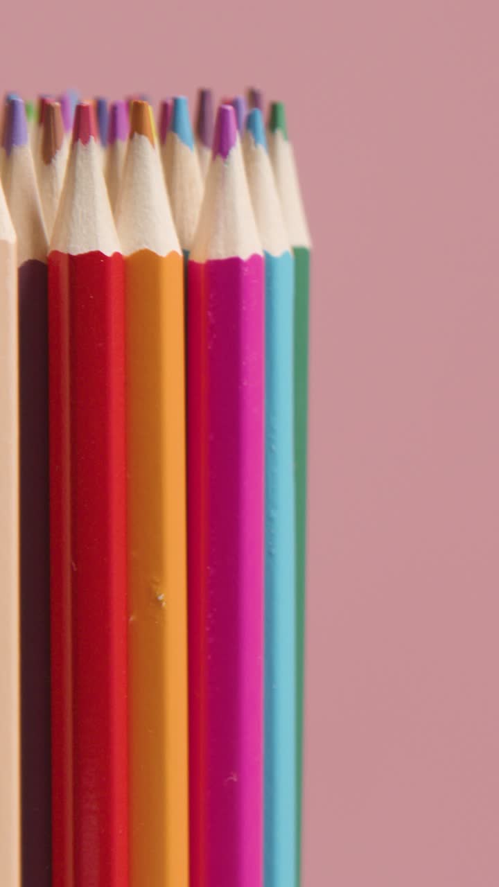 fotografía vertical de estudio de lápices multicolores giratorios contra un fondo rosado 1