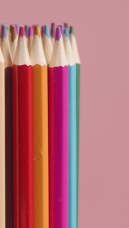 fotografía vertical de estudio de lápices multicolores giratorios contra un fondo rosado 1