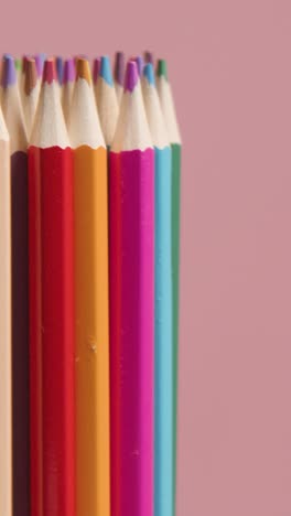 vertical video studio shot of rotating multi-coloured pencils against pink background 1