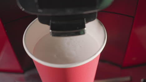 close up of coffee machine dispensing foamy milk into red paper cup. soft foam swirling in cup, ideal for cafe, coffee preparation, barista art, or milk-based beverages