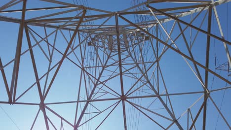 electricity transformer tower on a blue sky backdrop with electric cable wires lines underneath look up view