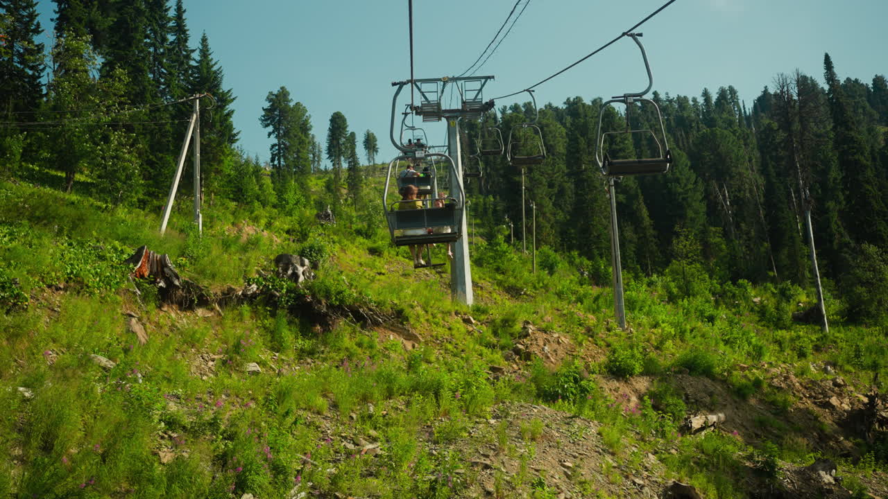 Tourists lift to top of mountain on cable car in summer. Enjoying leisure time together on holiday. Hotel area surrounded by hills and forest slow motion