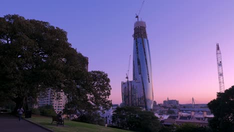 Man-sits-at-park-bench-under-Skyscraper