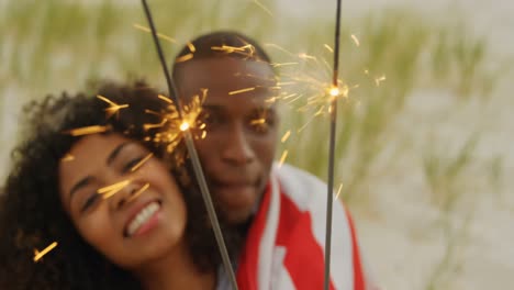 vista frontal de una pareja afroamericana con chispas en las manos en la playa 4k