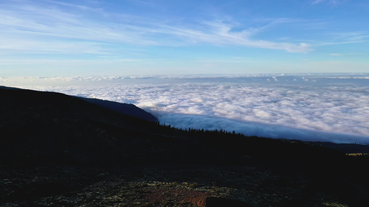 Hikers climbing on a cliff below Pico de Teide on Tenerife followed by a drone flying above a dense cloud inversion in the valley and coastline below. Hikers watching a cloud inversion by the sea 4K.