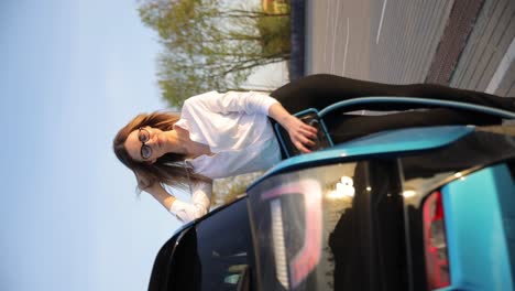 close-up of woman charging electric blue car at station. vertical video