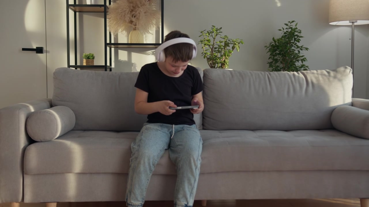 Un ragazzo con le cuffie è seduto su un divano e usa un tablet in una stanza soleggiata, in un'atmosfera di calma.