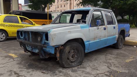 a rusty and dilapidated pickup truck with a flat tire parked on a city street next to a yellow taxi.