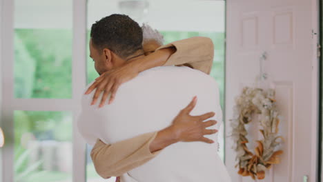 adult son greeting senior mother as she arrives to celebrate christmas at home