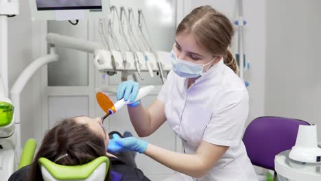 Young-female-dentist-in-mask-and-gloves-using-dental-UV-light-equipment-for-polymer-hardening