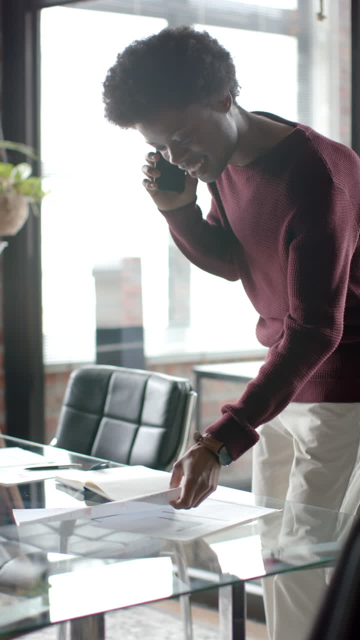 African American man talks on phone, holds documents at home in slow-motion video