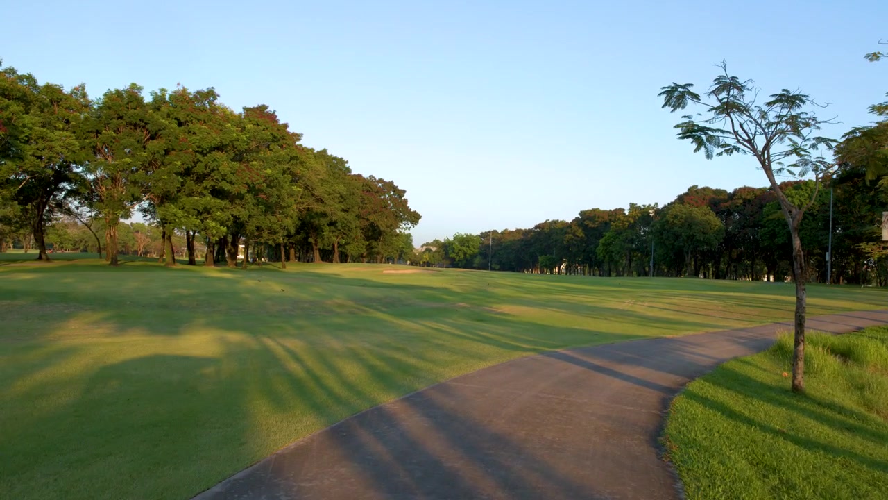 Wide panning shot of a curved asphalt path through a sunny tropical park landscape.