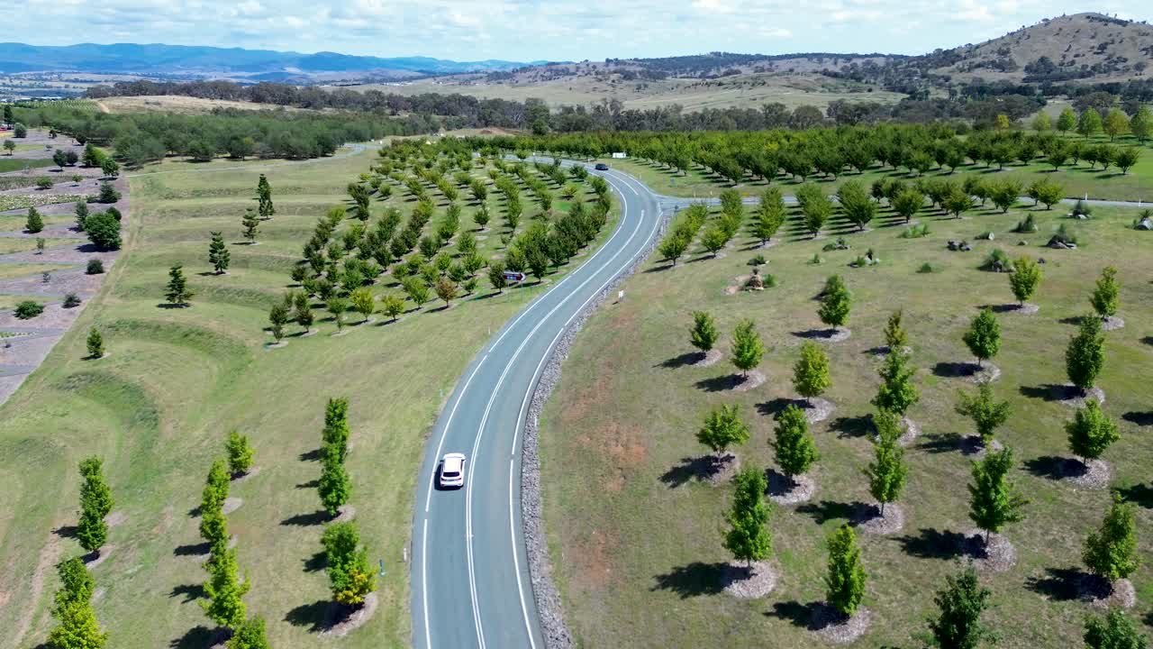 Drone aerial landscape of car vehicles and bicycle rider driving down winding road street in vineyard valley region with trees National Arboretum Canberra ACT Australia industry outdoors transport