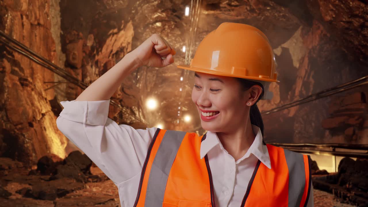 Close Up Of Asian Female Engineer With Safety Helmet Flexing Her Bicep And Smiling To Camera In Underground Mine Tunnel