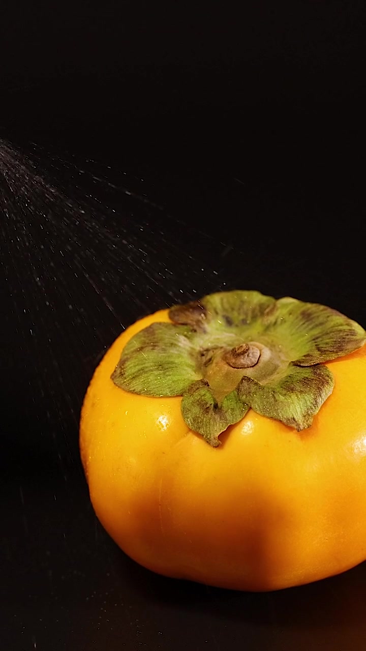 Tangan menyemprotkan air pada buah kesemek