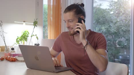 el hombre está sentado en su computadora portátil y haciendo una llamada telefónica, entorno doméstico interior, trabajo remoto y concepto de teletrabajo