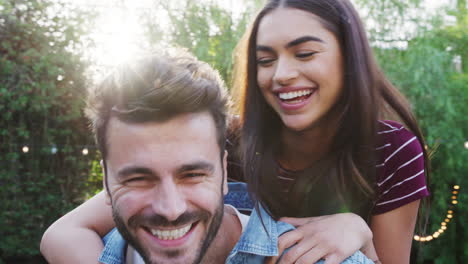 portrait of couple with man giving woman piggyback at home in back garden