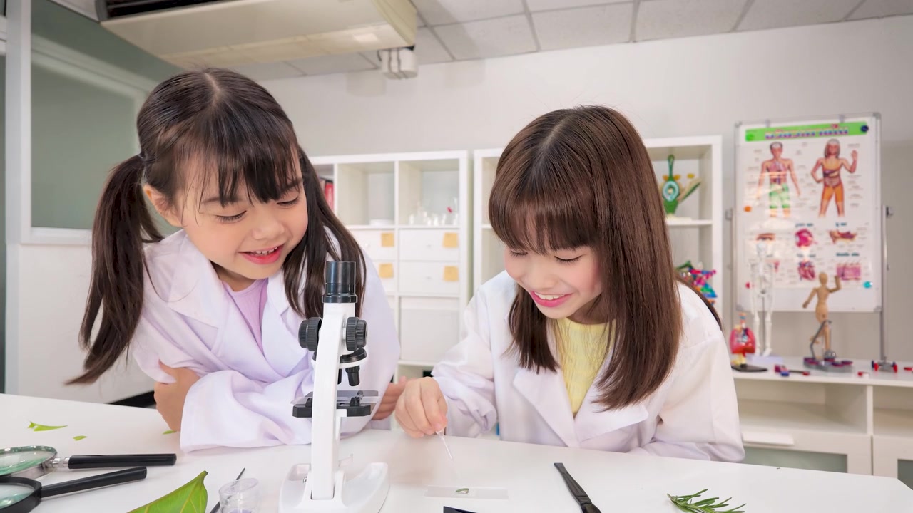 教室で、白衣を着た2人の若い学生が顕微鏡を使って標本を観察している