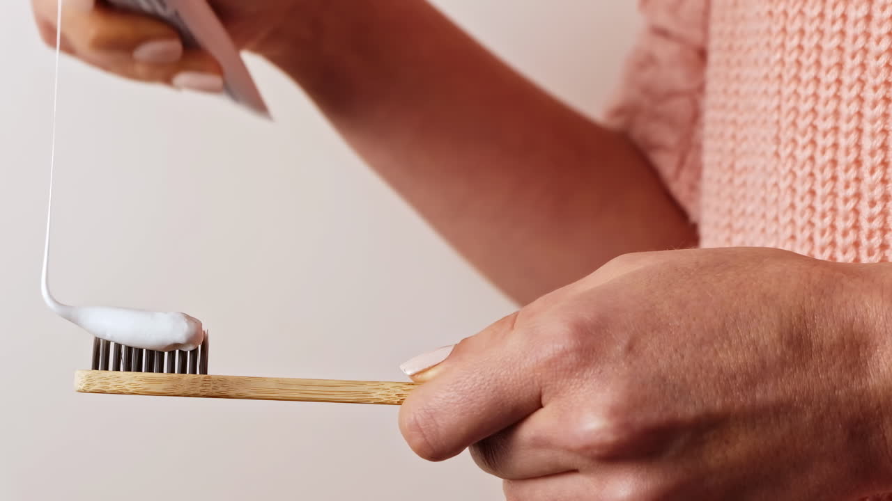 Woman hands pours toothpaste on bamboo toothbrush