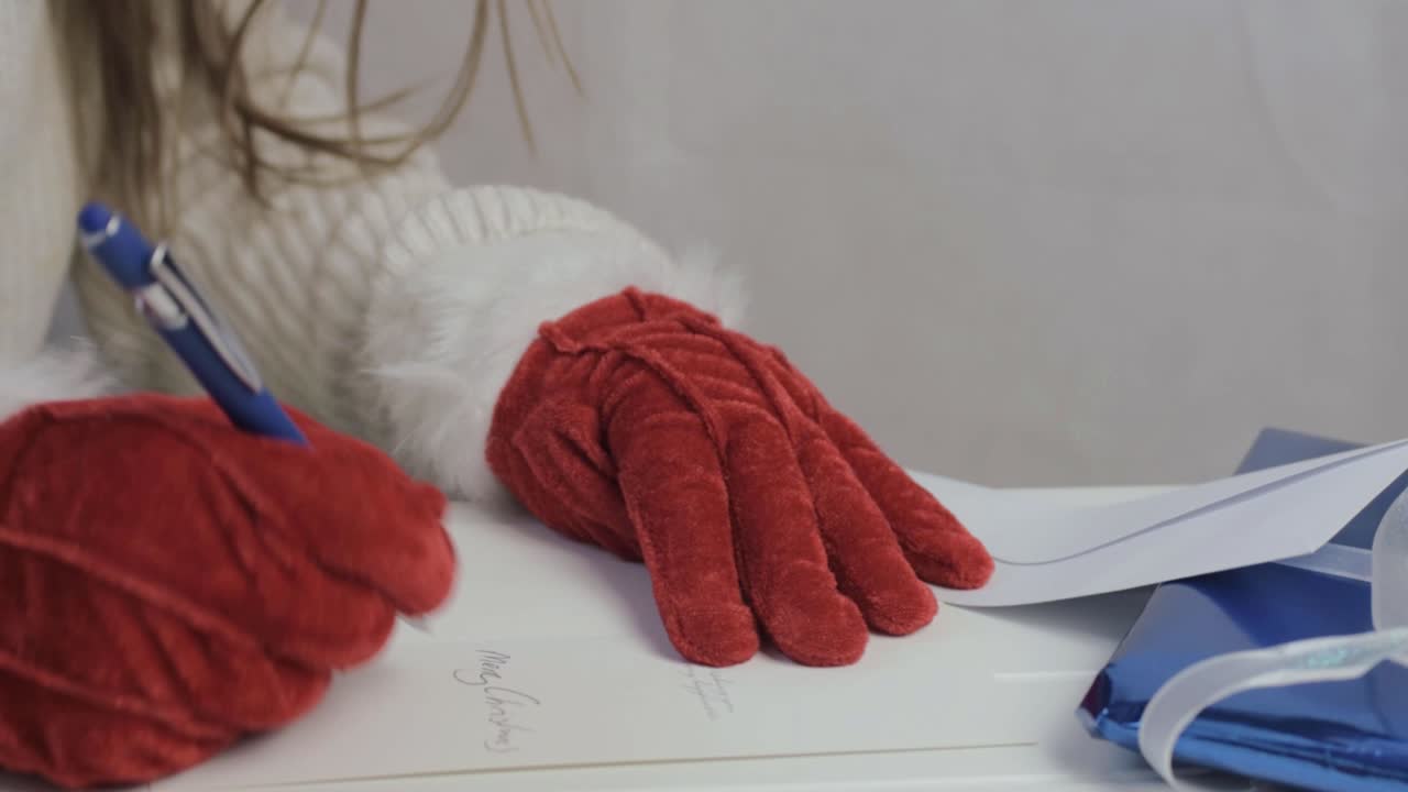 Woman writing out Christmas greeting cards wearing red Santa gloves medium shot